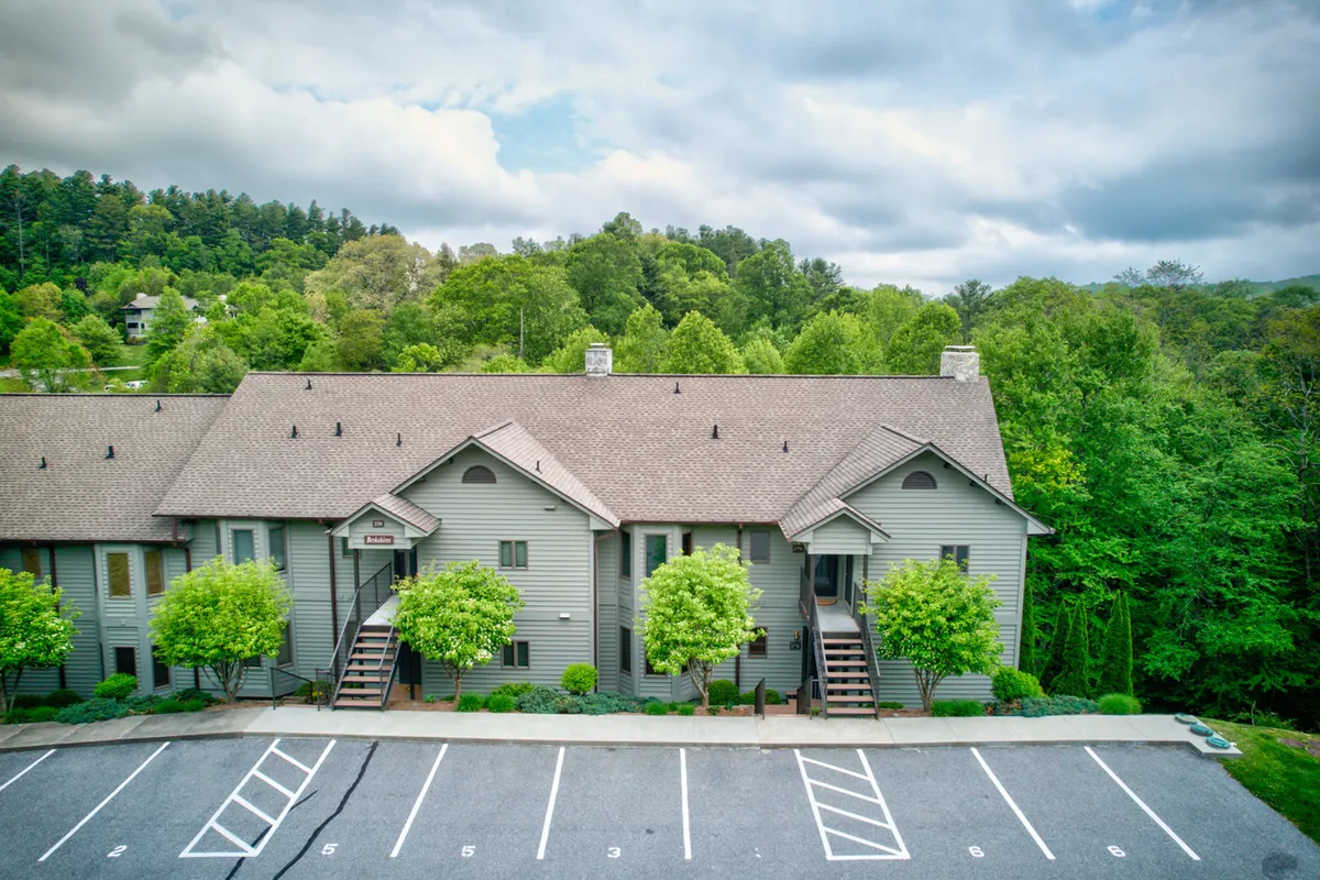 A welcoming exterior shot of the resort townhomes, framed by green trees and an inviting sunset sky. Balconies overlook open spaces, with the parking lot in view, suggesting easy access and a community atmosphere ideal for seasonal events and outdoor relaxation.