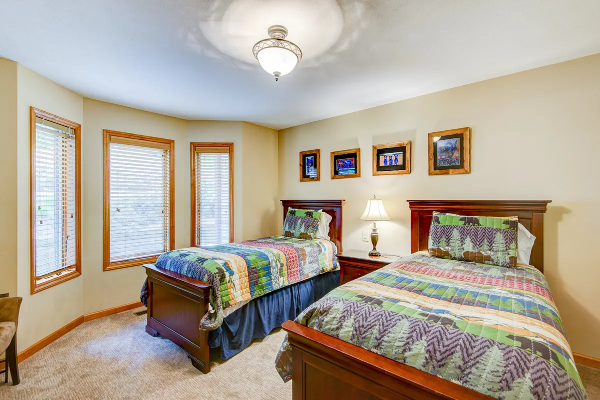A twin bedroom is pictured here, with two beds featuring colorful quilts, decorative wall frames above, and a central table lamp. The decor is playful yet comfortable, ideal for kids or friends sharing a room.