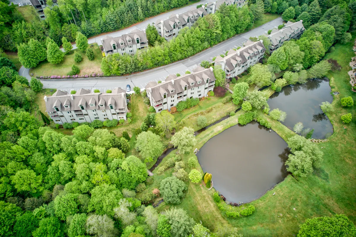 A tranquil pond surrounded by residential buildings and verdant greenery, capturing the calm of the community's outdoor spaces. The sunset reflection on the pond and dew on the grass hint at a variety of ways to enjoy nature throughout the seasons.