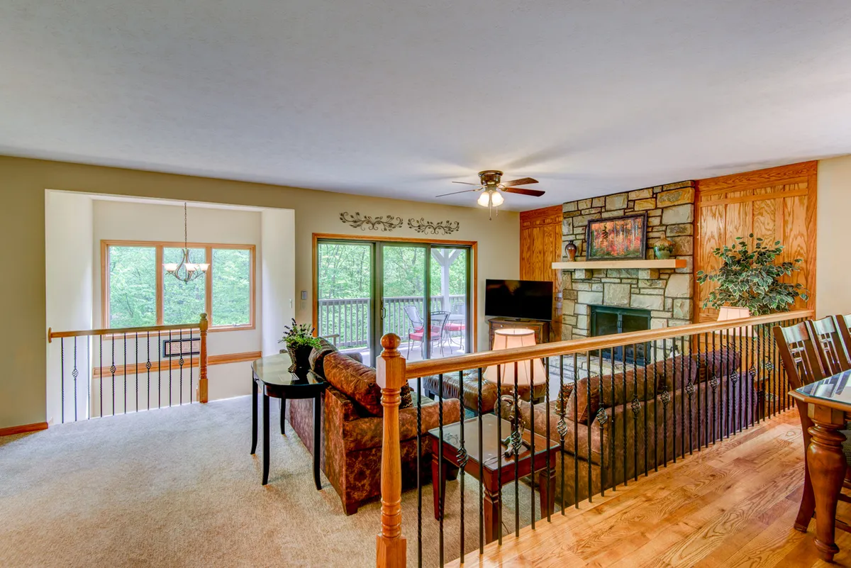 The image shows a welcoming living room with a stone fireplace, large windows providing natural light, comfortable seating, and a wooden dining table. The decor is inviting and perfect for family gatherings or entertaining guests.