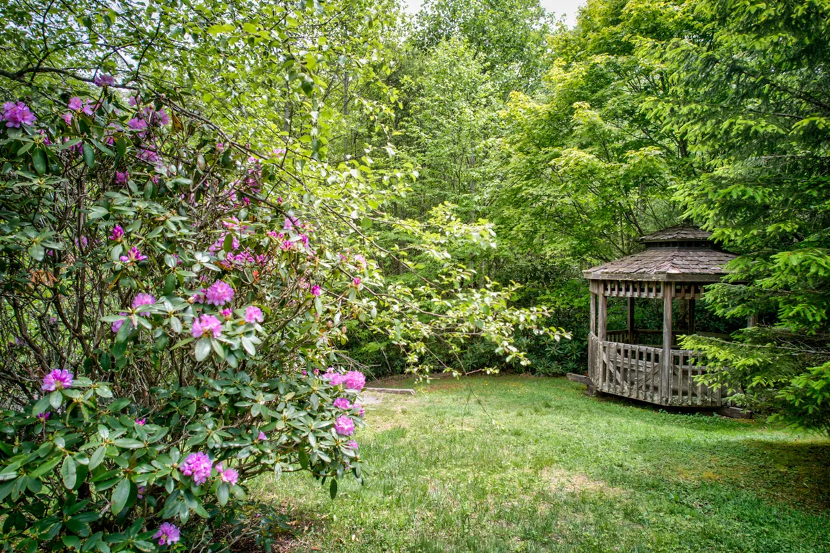 A peaceful gazebo nestled among flowering shrubs and lush greenery, ideal for small outdoor gatherings, relaxing, or sharing morning coffee together. The area invites guests to enjoy the outdoors in a communal setting.