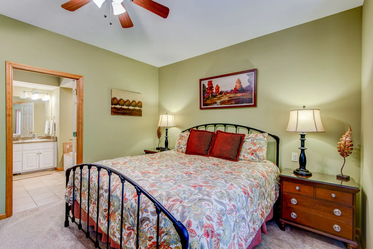 The image features a bedroom with a comfortable bed adorned in colorful bedding, a nightstand with a lamp, and framed artwork on the wall. The room exudes warmth and comfort, ideal for unwinding after a long day.