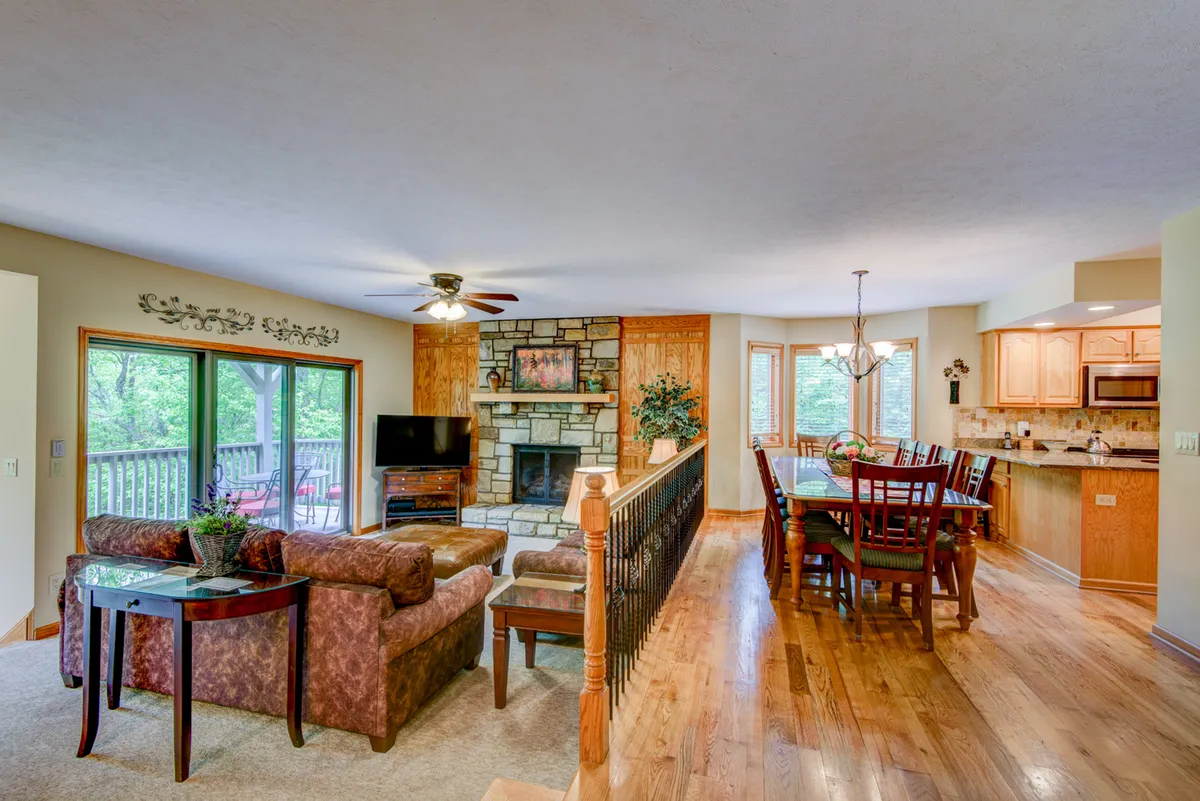 A wide-angle shot of the main living space featuring a striking stone gas log fireplace, a large dining table that seats ten, and expansive windows that fill the space with natural light. Comfortable seating and tasteful décor create a welcoming atmosphere perfect for gatherings.