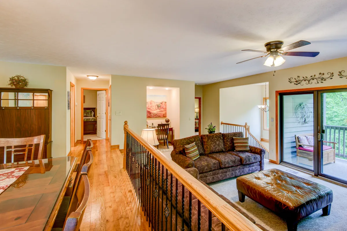 A cozy interior shot with a sofa, dining table, and sliding door opening to a private deck. Morning light streams in, suggesting a seamless connection between indoor and outdoor living spaces.