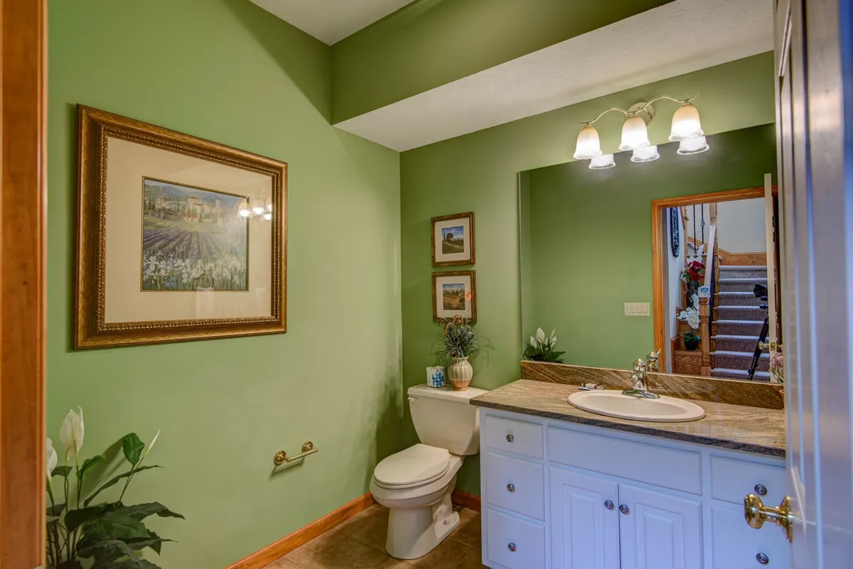 This interior image highlights a half bath with a fresh green wall, framed artwork, a mirror, vanity, and toilet. The setting is clean, modern, and easily accessible, supporting the den’s functionality for groups or overnight guests.