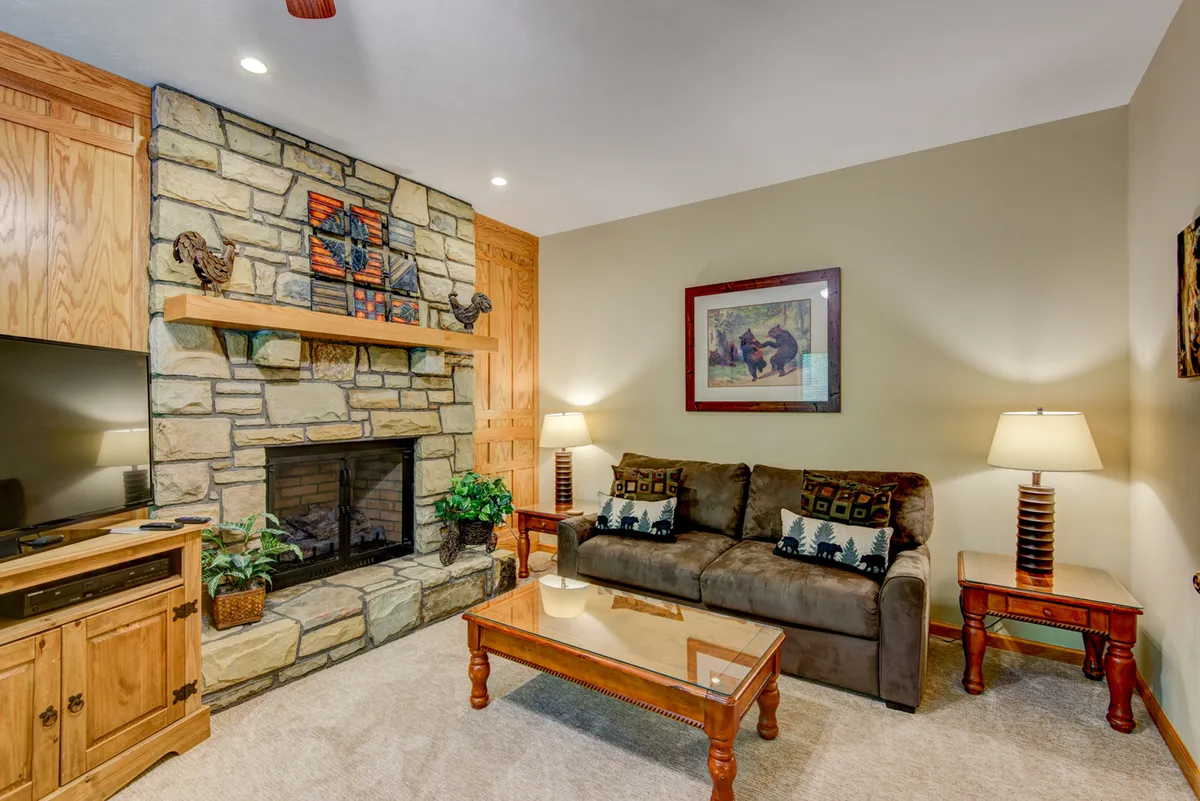 This photo presents another angle of a den-like living space, focusing on the cozy stone fireplace, a plush couch, and wooden furnishings. Artwork and soft lighting add a welcoming, home-like touch—ideal for quiet downtime, reading, or group gatherings. While the foosball table isn’t visible here, the fireplace and seating reinforce the den’s cozy and versatile appeal.